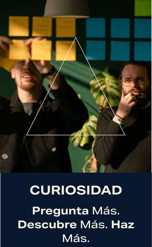 Curiosidad. PRegunta Más. Descubre Más. Haz Más. Dos compañeros de trabajo realizando una lluvia de ideas sobre una pizarra.